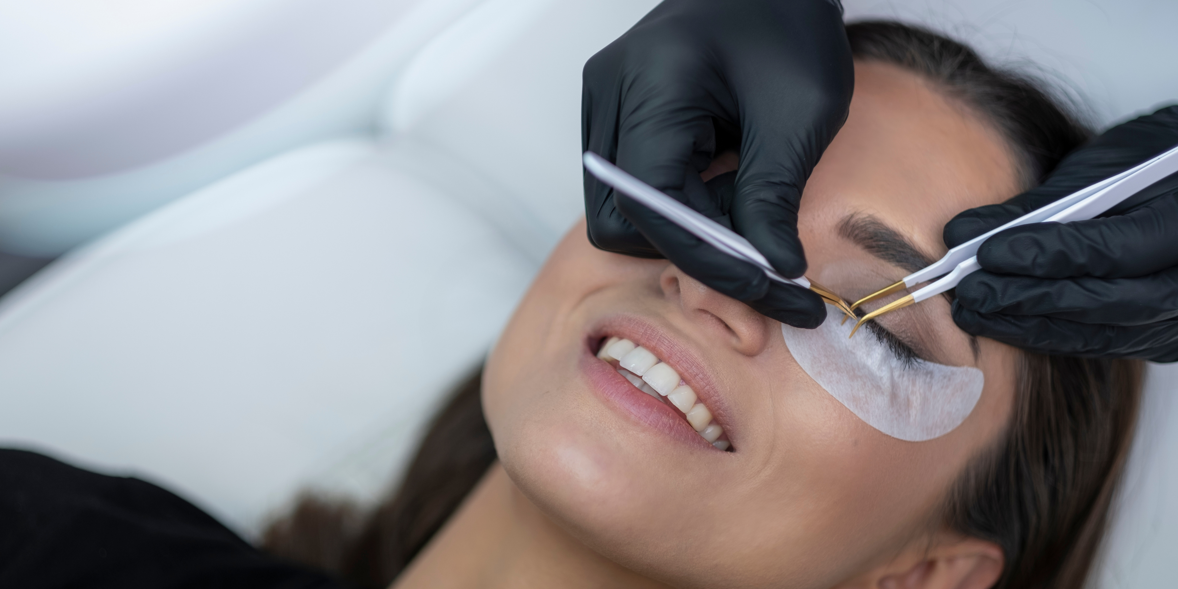 woman having eyelash extensions applied - her eyes are closed - she is smiling