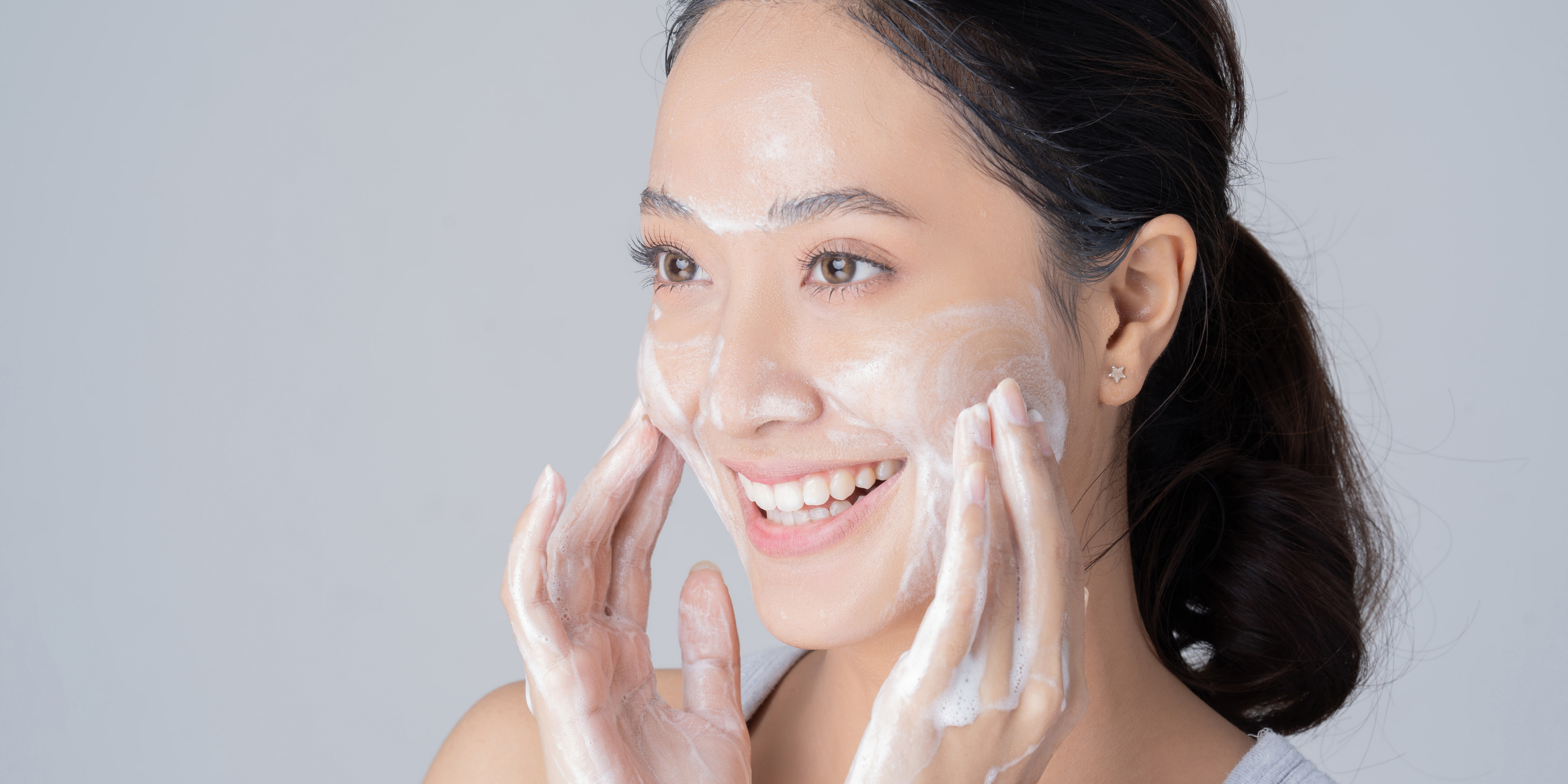 woman cleansing her skin with a foaming cleaner - making sure she is makeup free for her eyelash extensions appointment